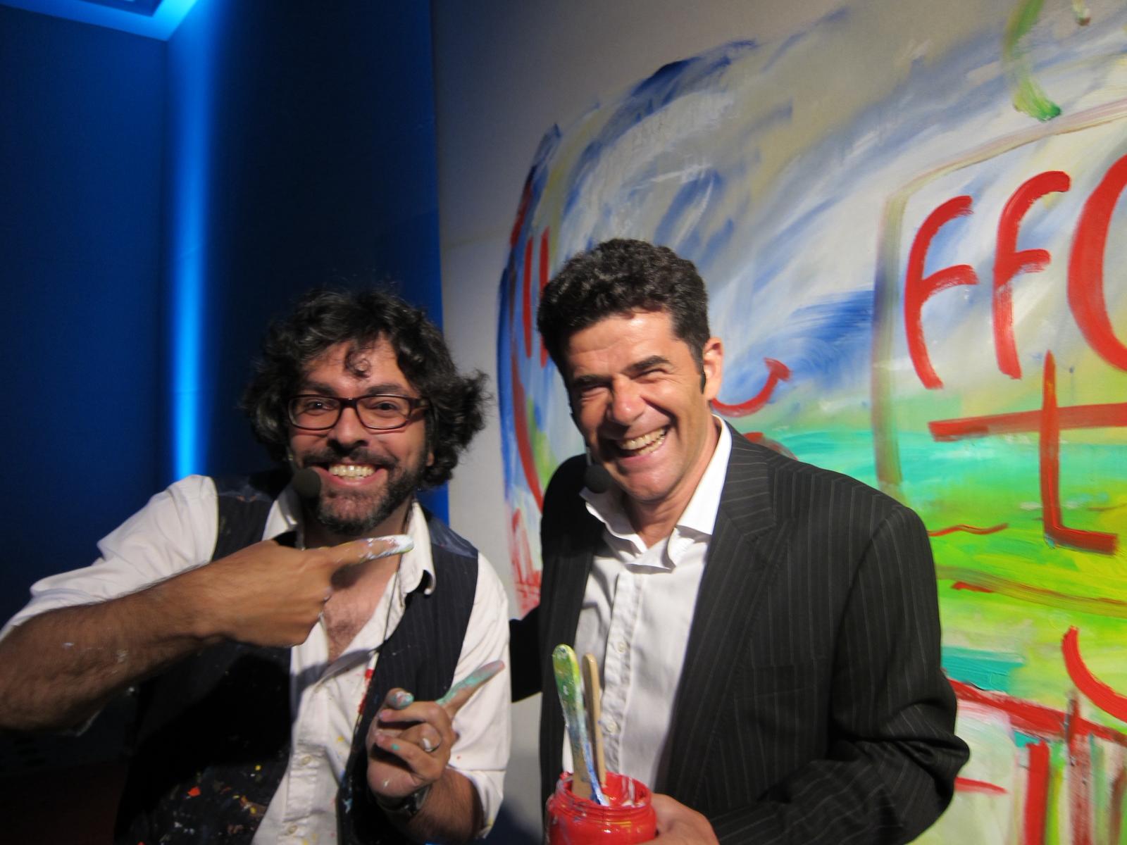 Liniers smiling beside a gala host with the painting visible behind them