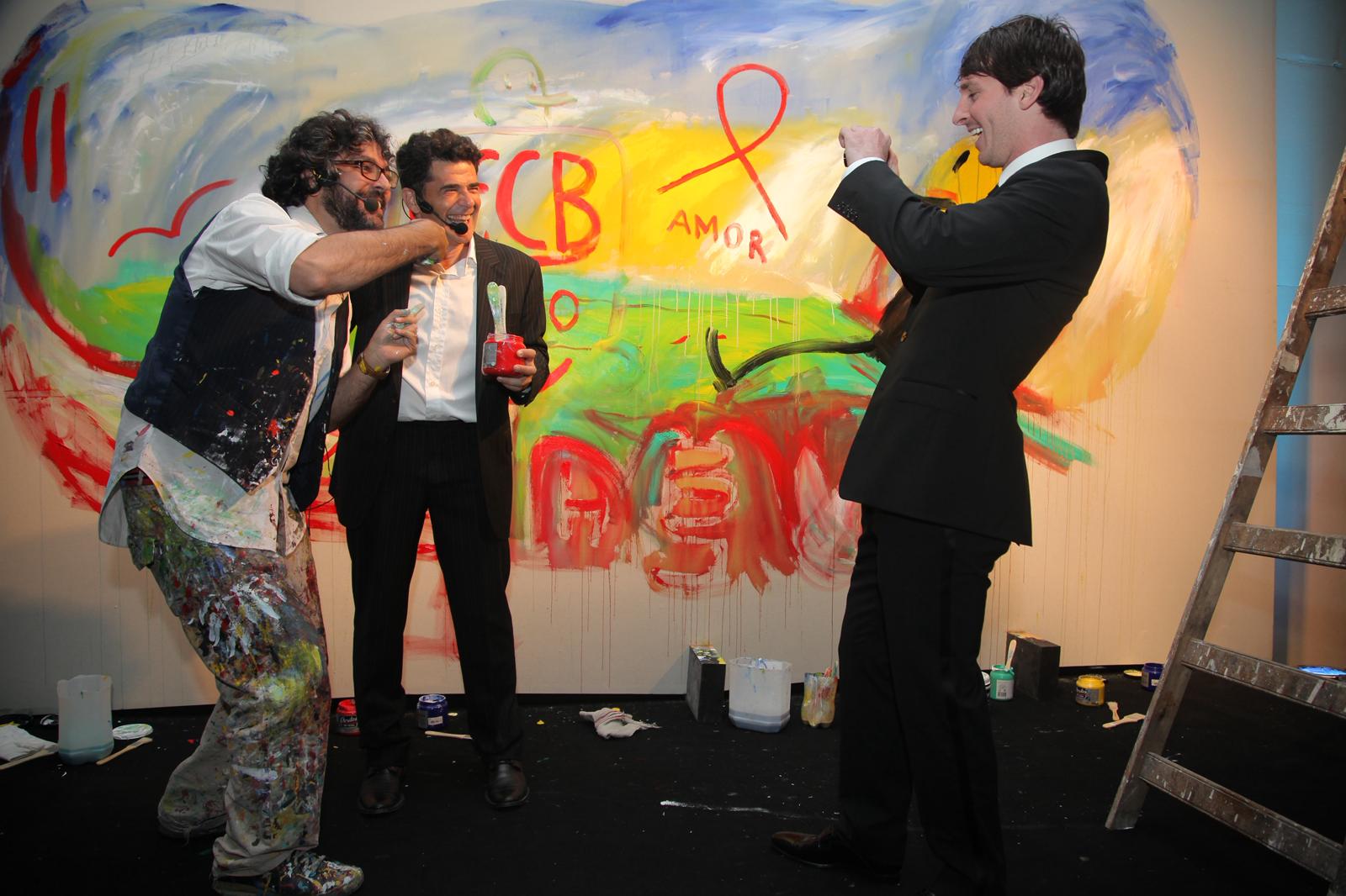 Liniers, a gala host, and Leo Messi standing in front of the artwork during the 2011 Fundación Messi event
