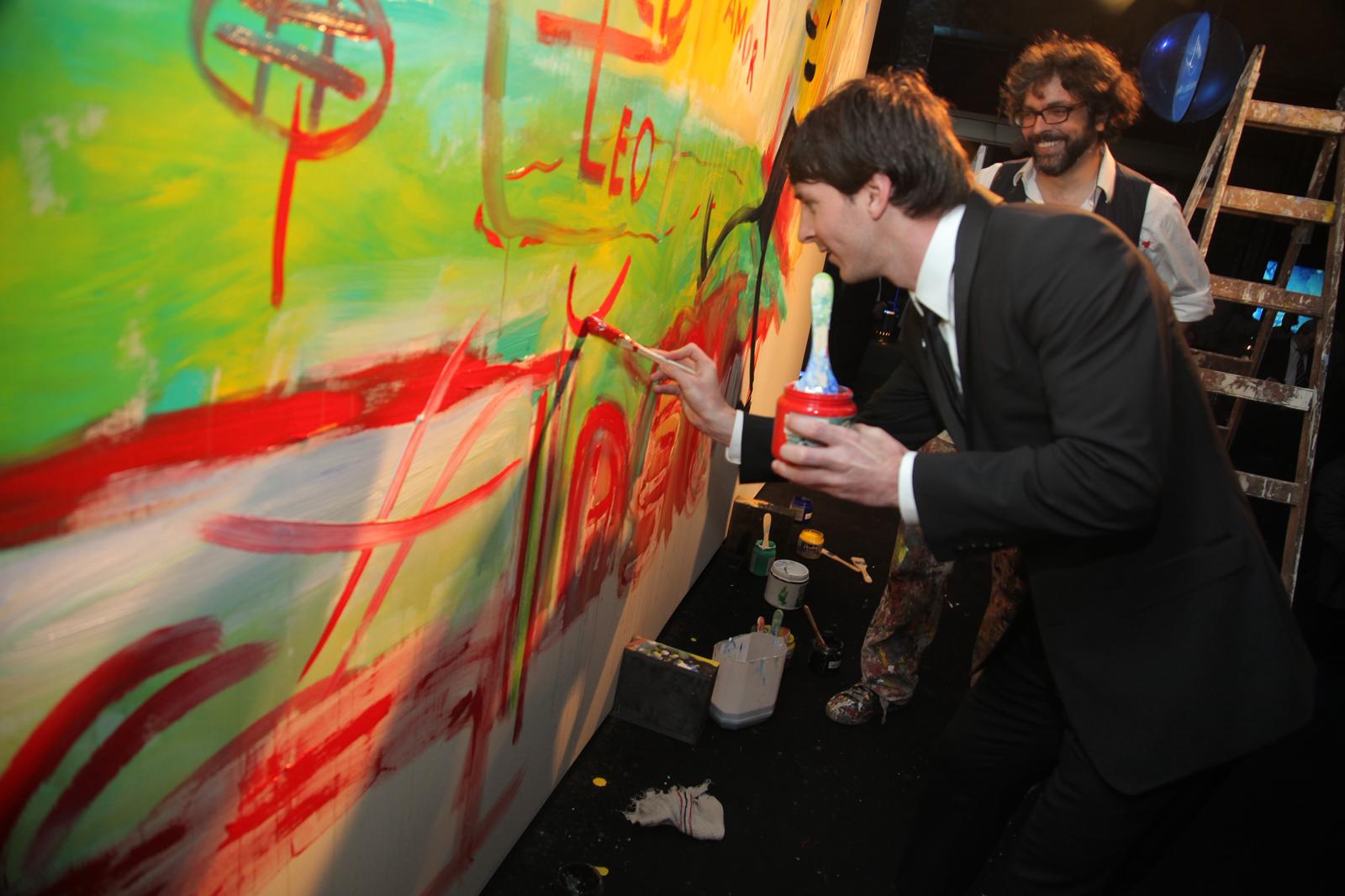 Leo Messi adding red paint to the large artwork during the 2011 Fundación Messi gala